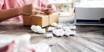 Young business start up online seller owner using computer for checking the customer orders from email or website and preparing packages for product office equipment.